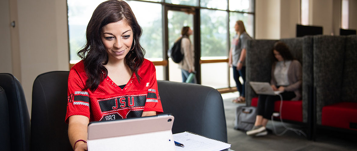 A student in the Houston Cole library working on her iPad and taking notes on paper